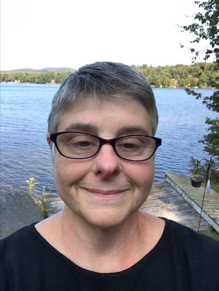 Caroline smiles in front water body and green deciduous trees